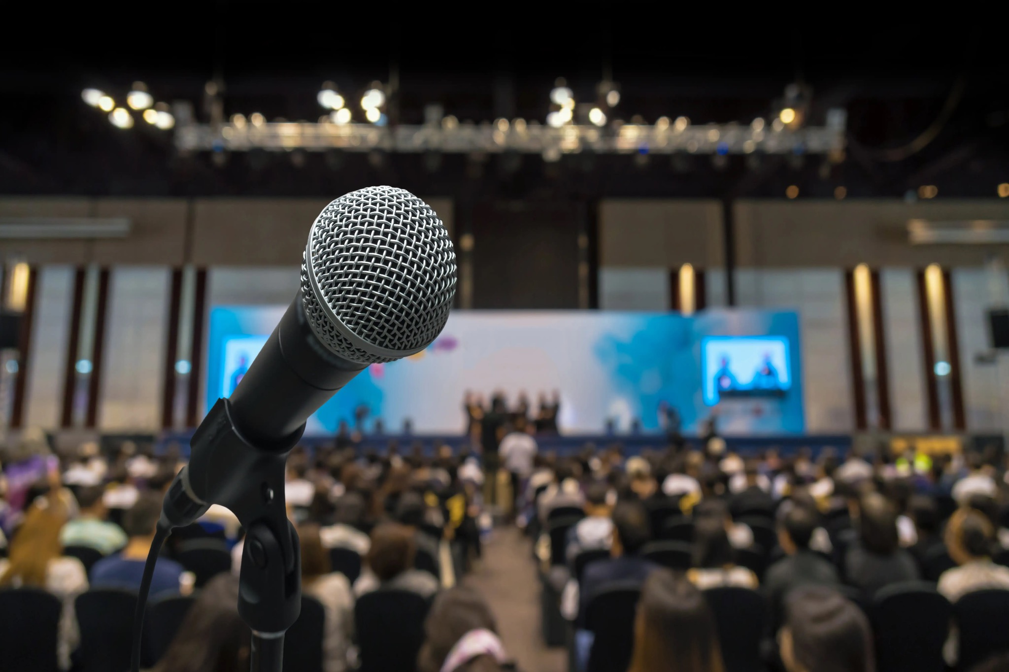 Microfone em destaque com plateia desfocada ao fundo em conferência
